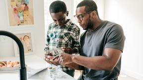 Parent counting money with child in kitchen. 