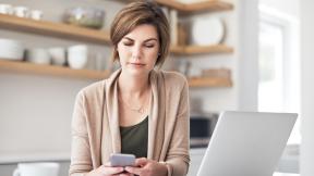 A woman looking at her phone and computer. 