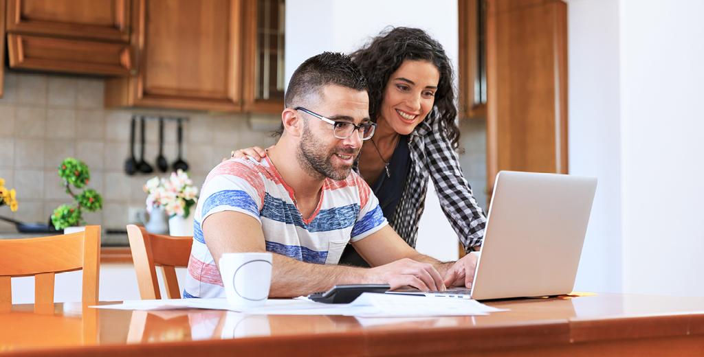 A guy and girl looking at a laptop in their kitchen. 