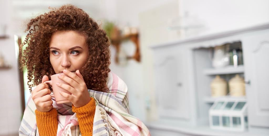 Girl wrapped up in a blanket with a coffee mug.